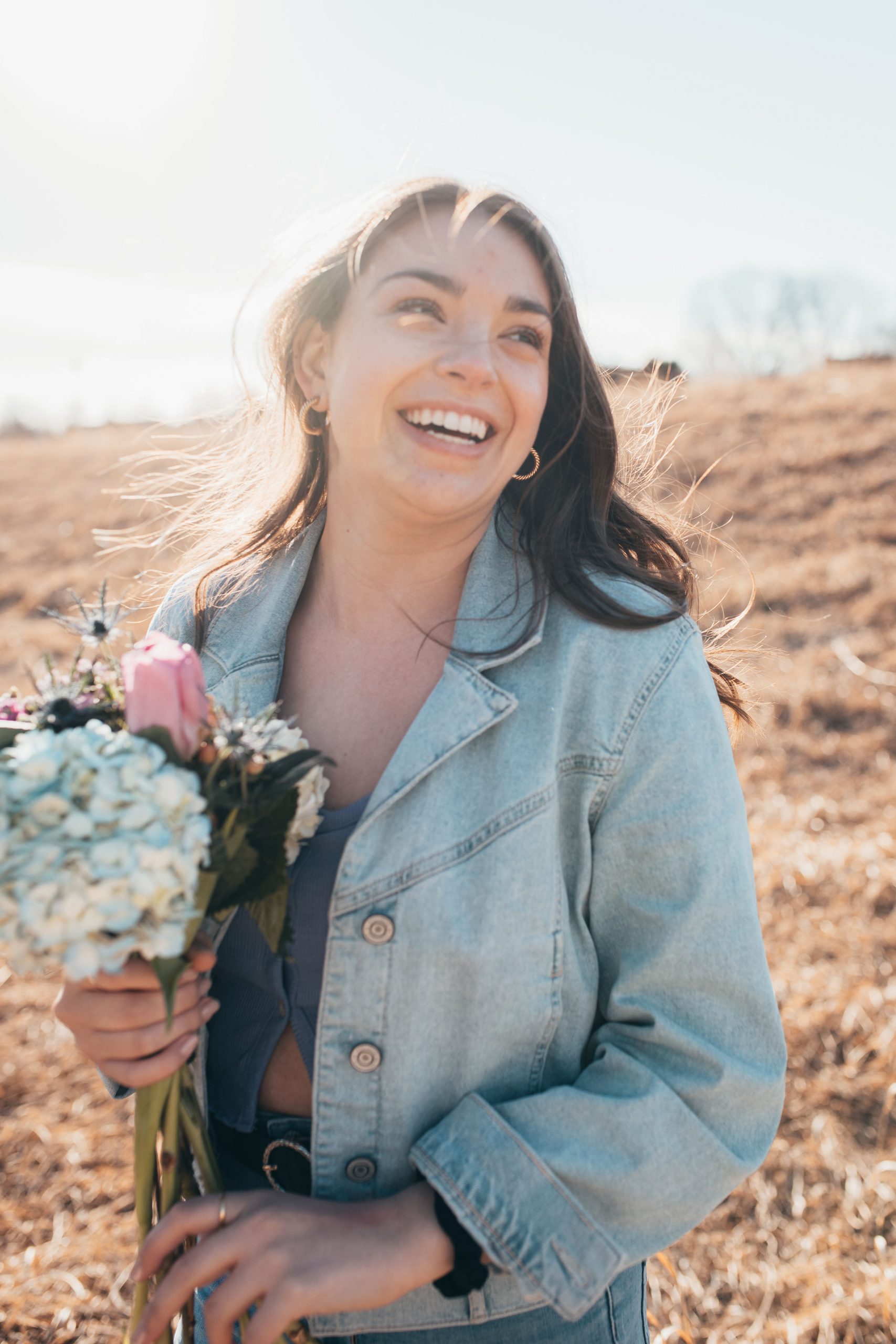 Angela LaRose- Open field, brown haired woman holds a bouquet of flowers while smiling